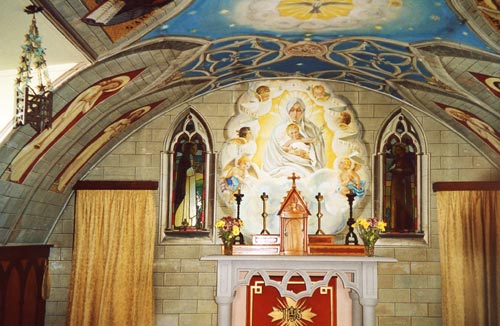 L’altare con la Madonna dell’Ulivo (da un’opera di Nicolò Barabino); a sinistra una delle lampade realizzate riciclando le scatolette di latta. Le tende in tessuto damascato che chiudono l’accesso alla sacrestia furono acquistate a Exeter con il fond